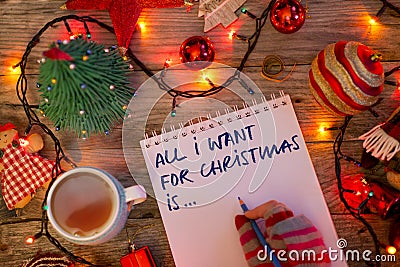 â€œAll I want for Christmas isâ€¦â€ text on notebook written by young woman with colorful gloves in festive decor Stock Photo